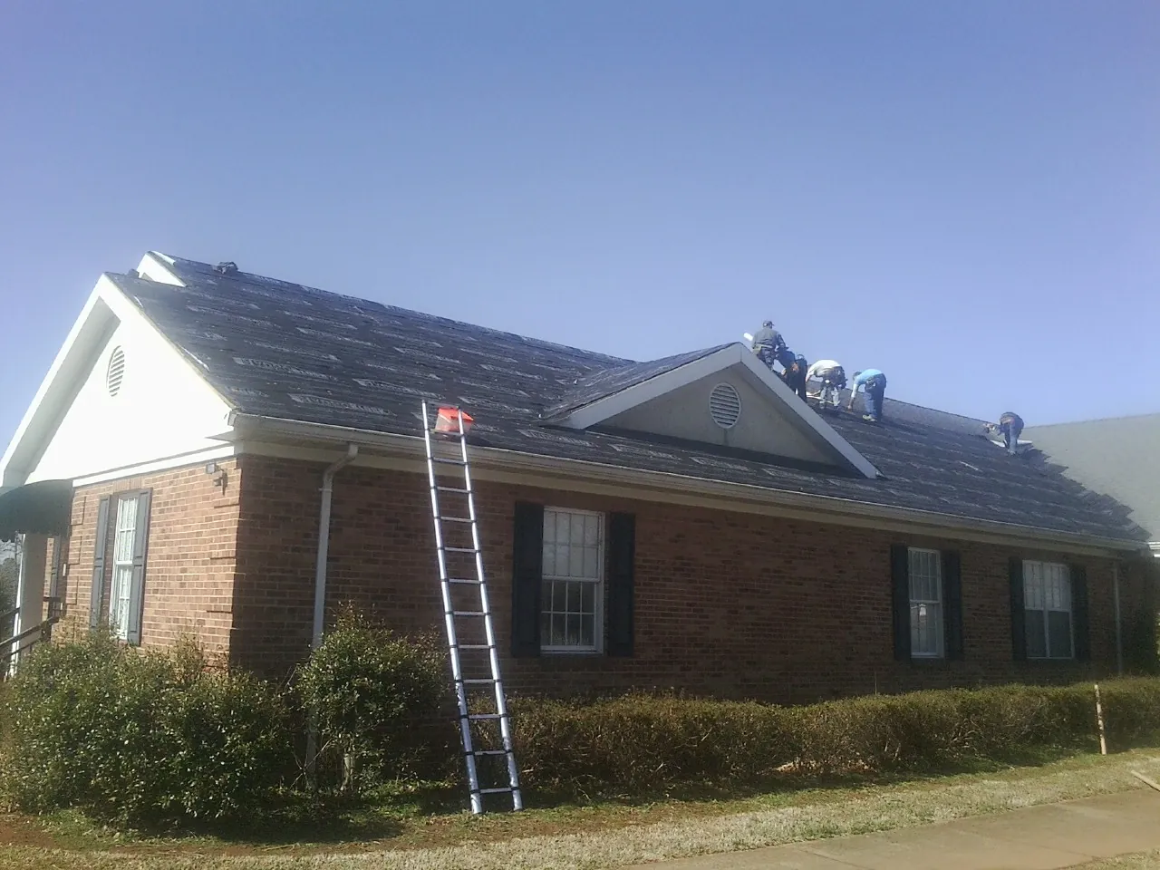 Crew tearing shingles off a brick ranch roof with a ladder set — Metal Roof Repair work by our crew in Center Sandwich
