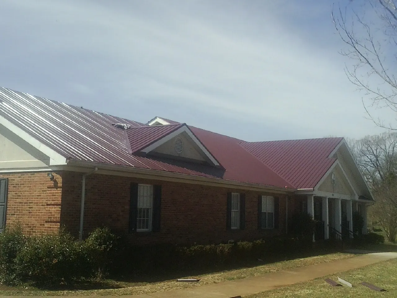 Red metal roof with gabled entries on a long brick building, from a Hail Damage Roof Repair job in Center Sandwich
