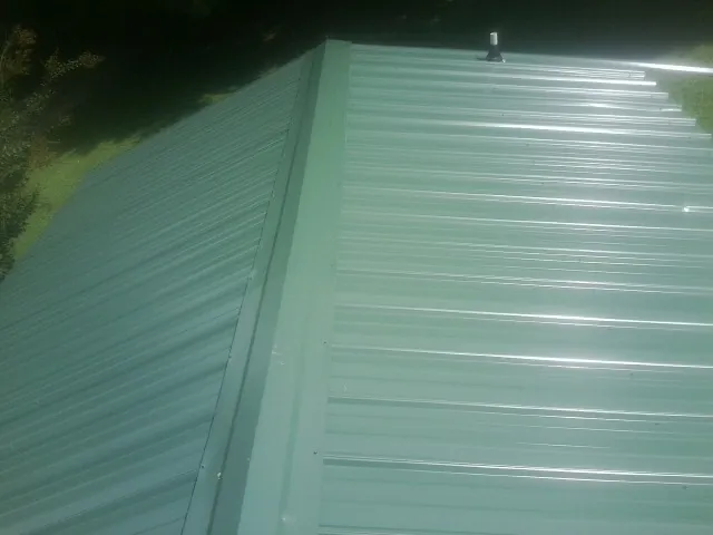New green metal panels meeting at the ridge of a roof — Flat Roof Repair work by our crew in Center Sandwich