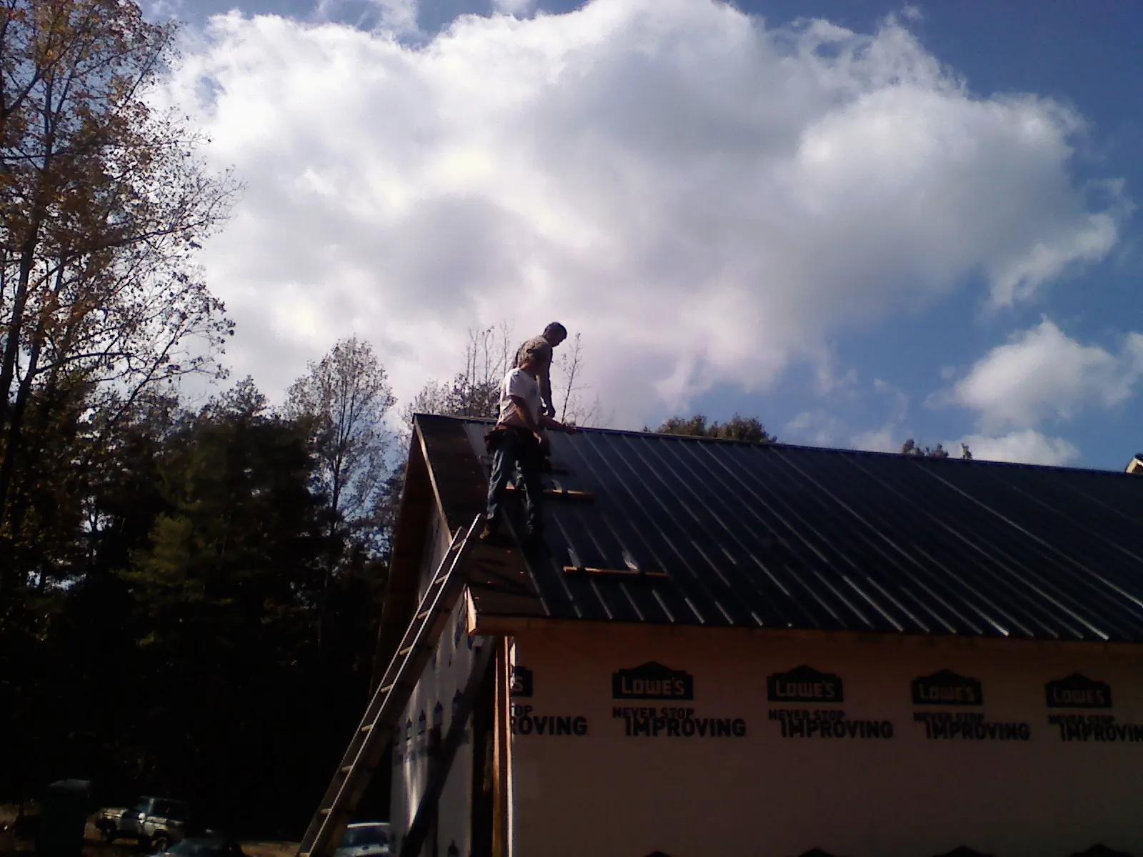 Roofer fastening dark metal panels high against a cloudy sky, from a Roof Inspection job in Center Sandwich