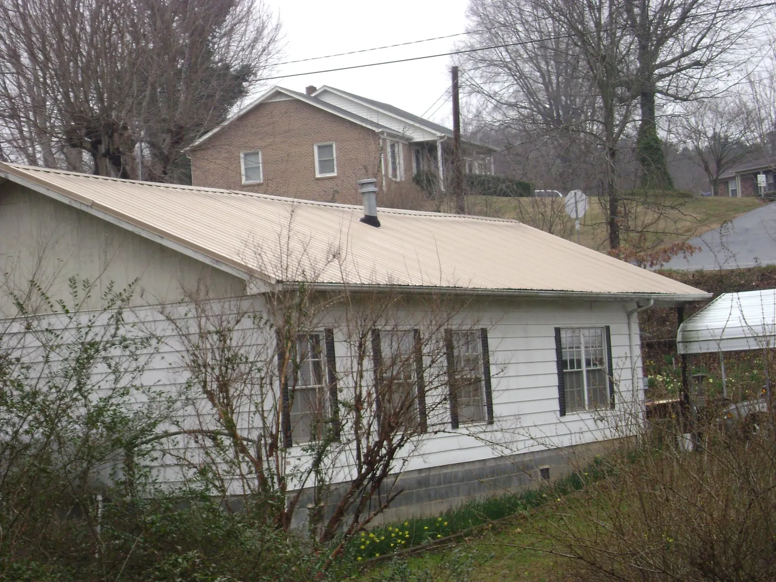 Tan metal roof on a white sided house set into a hillside — Commercial Roofing by Roofing Brothers in Center Sandwich