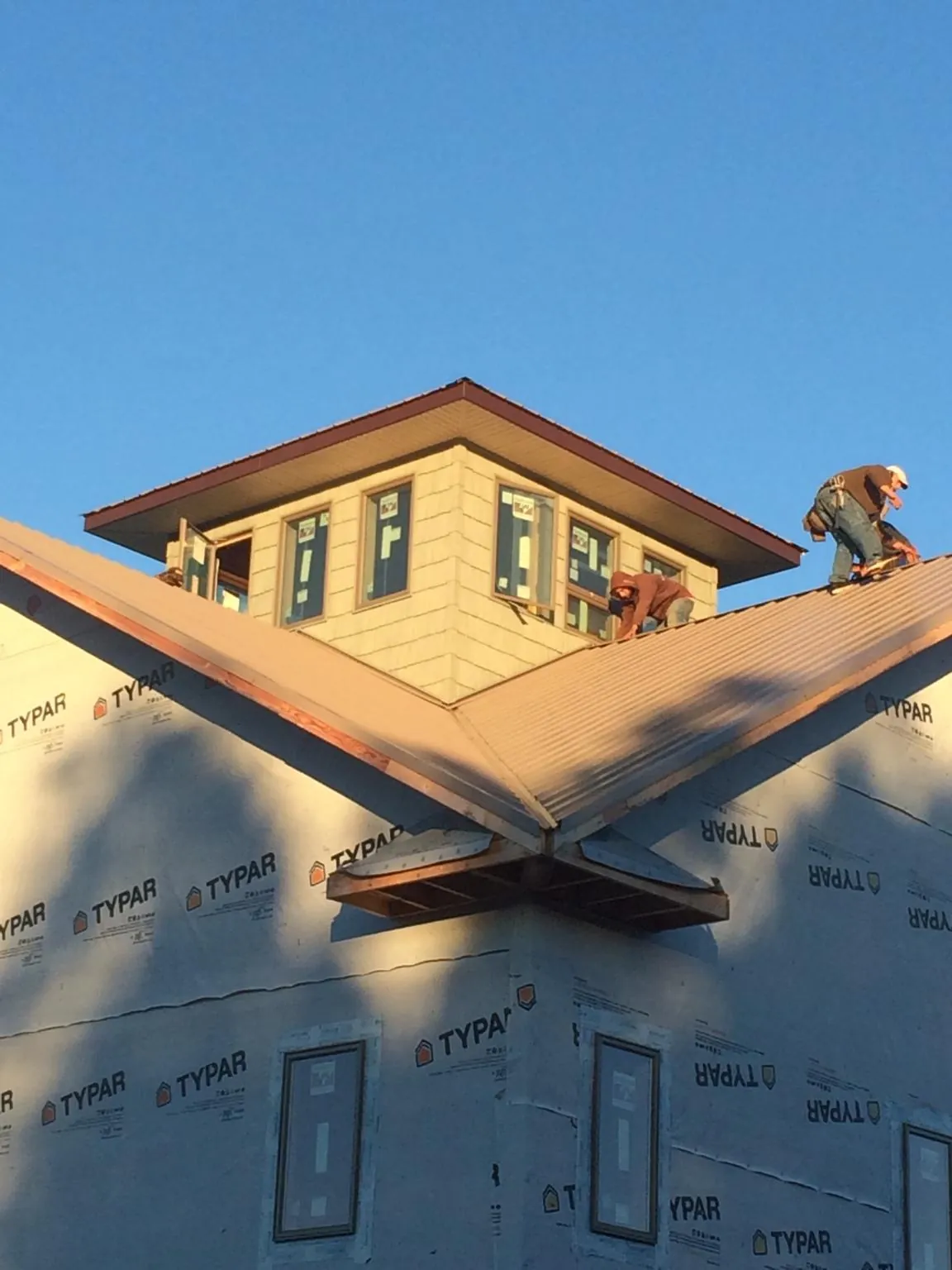 Roofers working around a rooftop cupola on a new metal roof at sunset — Roof Waterproofing in Center Sandwich by Roofing Brothers
